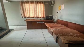 A reception desk with a sign, a sofa, a window with curtains, and a wall-mounted air conditioning unit.