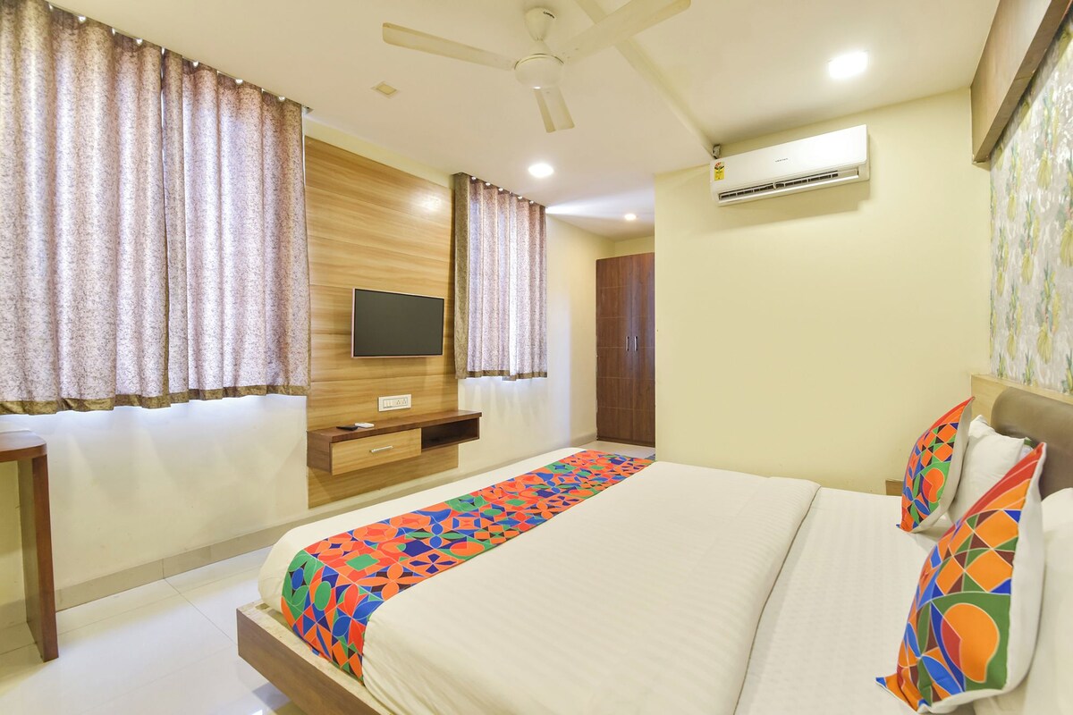 A hotel room with a bed, a TV mounted on the wall, an air conditioning unit, and a wardrobe.