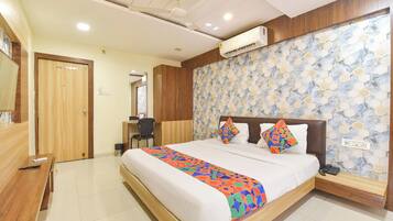 A hotel room with a bed, a desk, a chair, an air conditioning unit, and a wall with a geometric pattern.