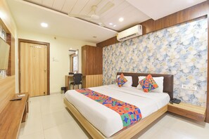 A hotel room with a bed, a desk, a chair, an air conditioning unit, and a wall with a geometric pattern. - FabHotel D9 (Indore)