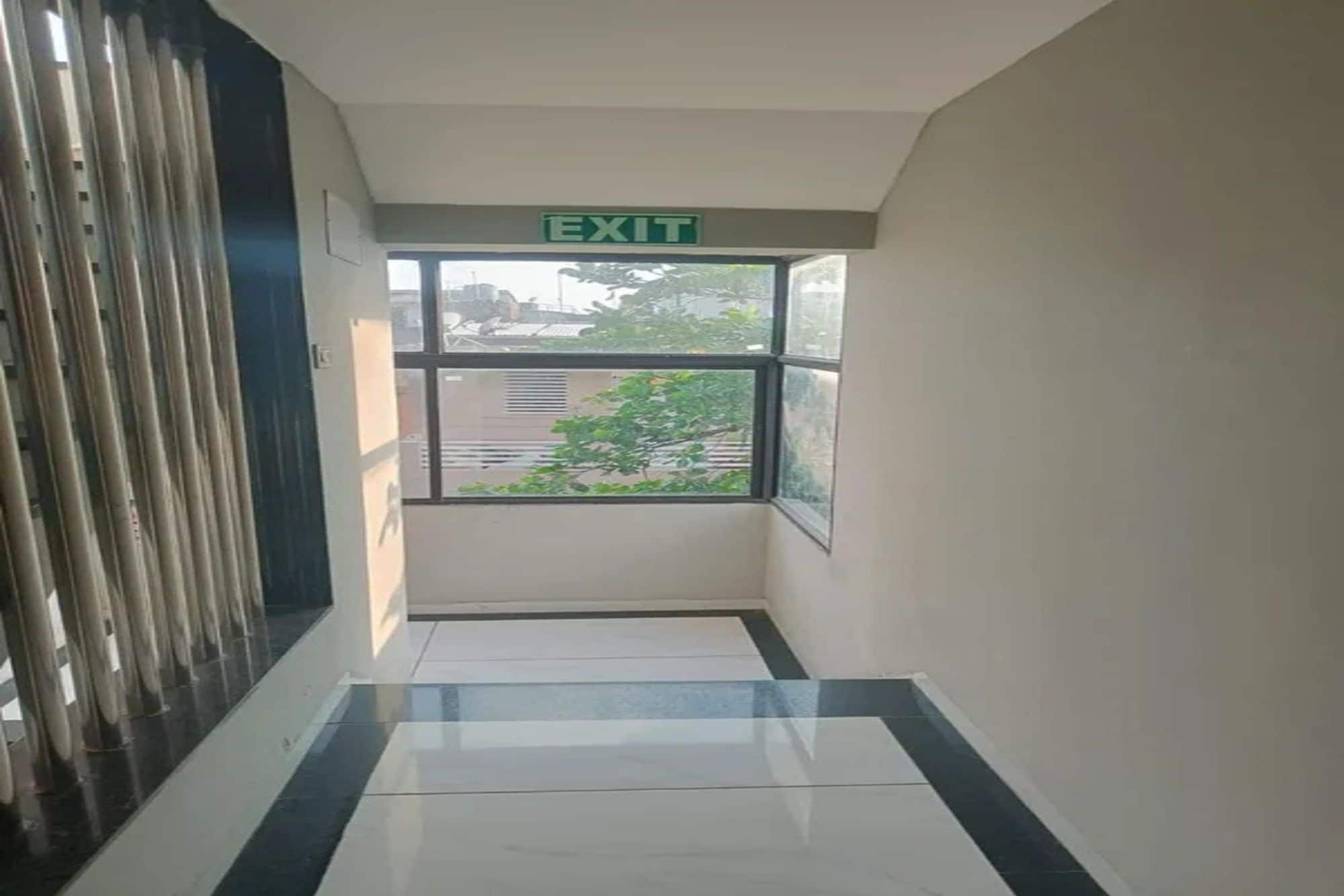 Un pasillo con una señal de salida, una ventana que ofrece vistas a edificios y árboles, y un piso de baldosas.
