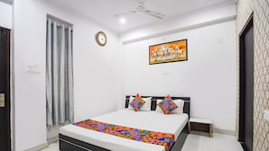 A bedroom with a bed, a painting, a ceiling fan, and a patterned curtain. - Fabhotel Golden Majestic (Prayagraj)