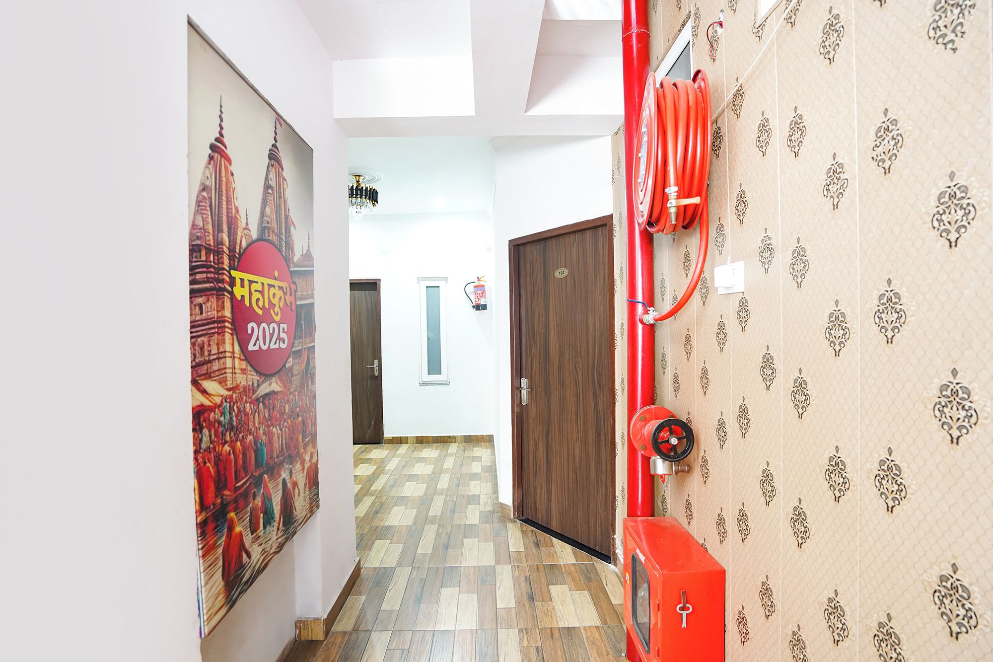 A corridor with patterned wallpaper, a red fire hose, and a door marked with the number 102.