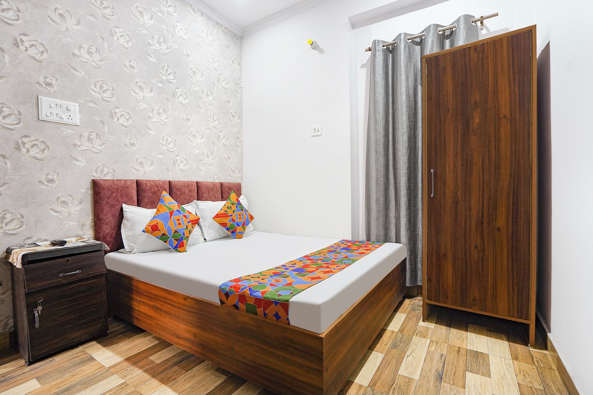 A bedroom with a wooden bed, a nightstand, a wardrobe, and a patterned wall.