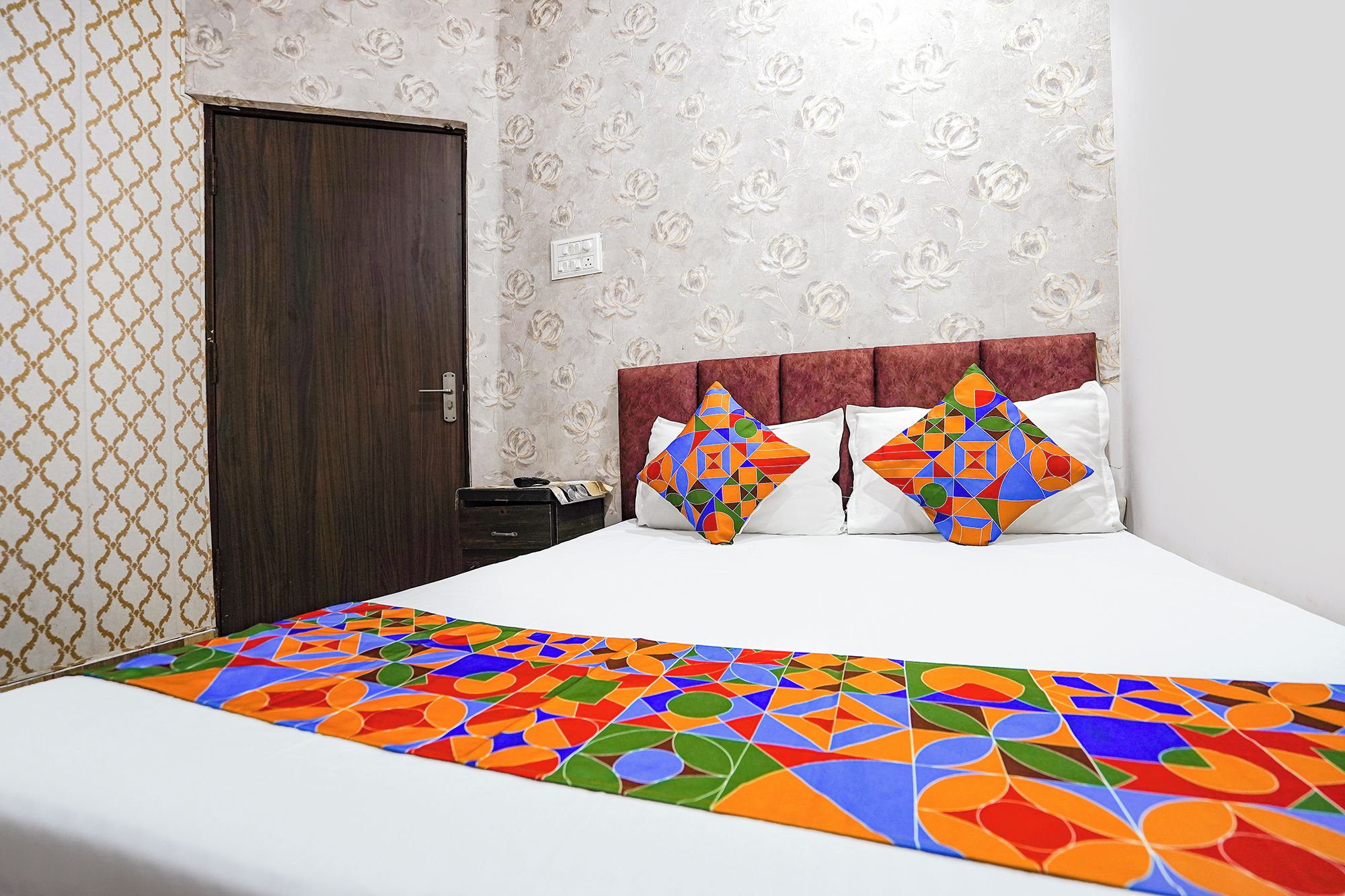 A hotel room with a bed, a headboard, a door, and patterned wallpaper.