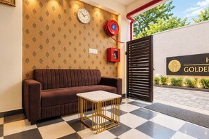 Ein Schachbrettmuster auf dem Boden, ein braunes Sofa, ein kleiner Tisch, eine Uhr, ein Feuerlöscher und ein verschlossener Eingang mit einem Schild.