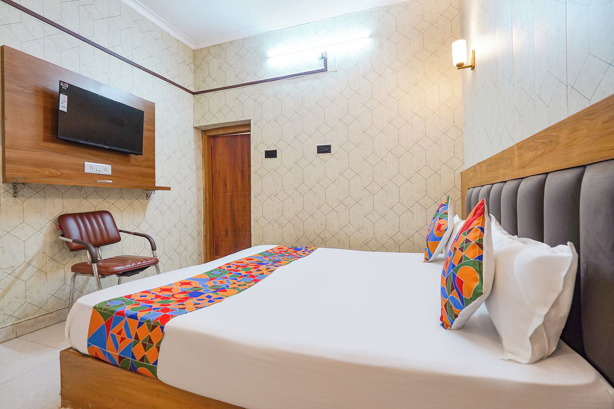 A hotel room with a bed, a TV mounted on the wall, a chair, and a door.