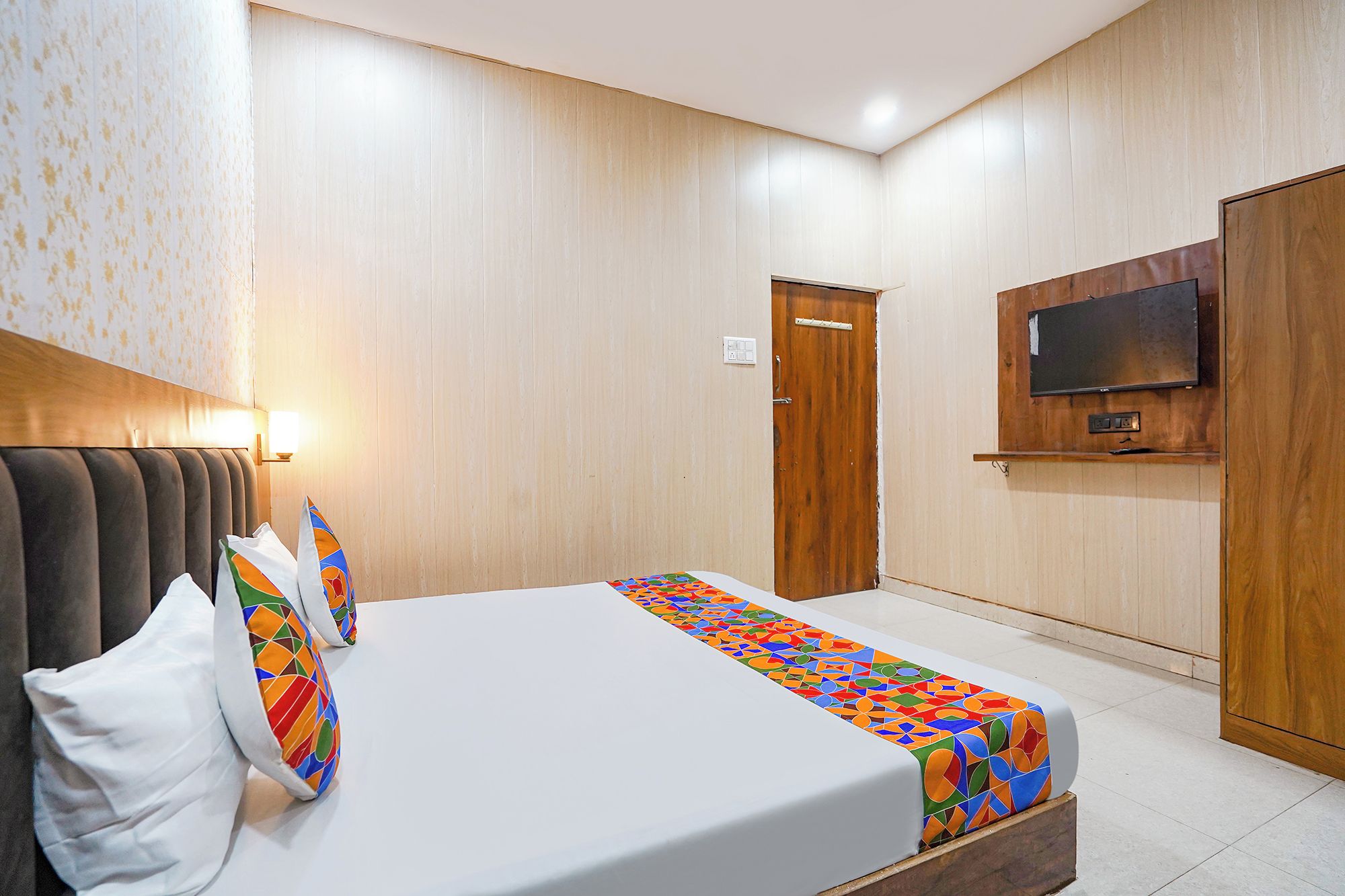 A hotel room with a bed, a television mounted on the wall, and a wooden door.