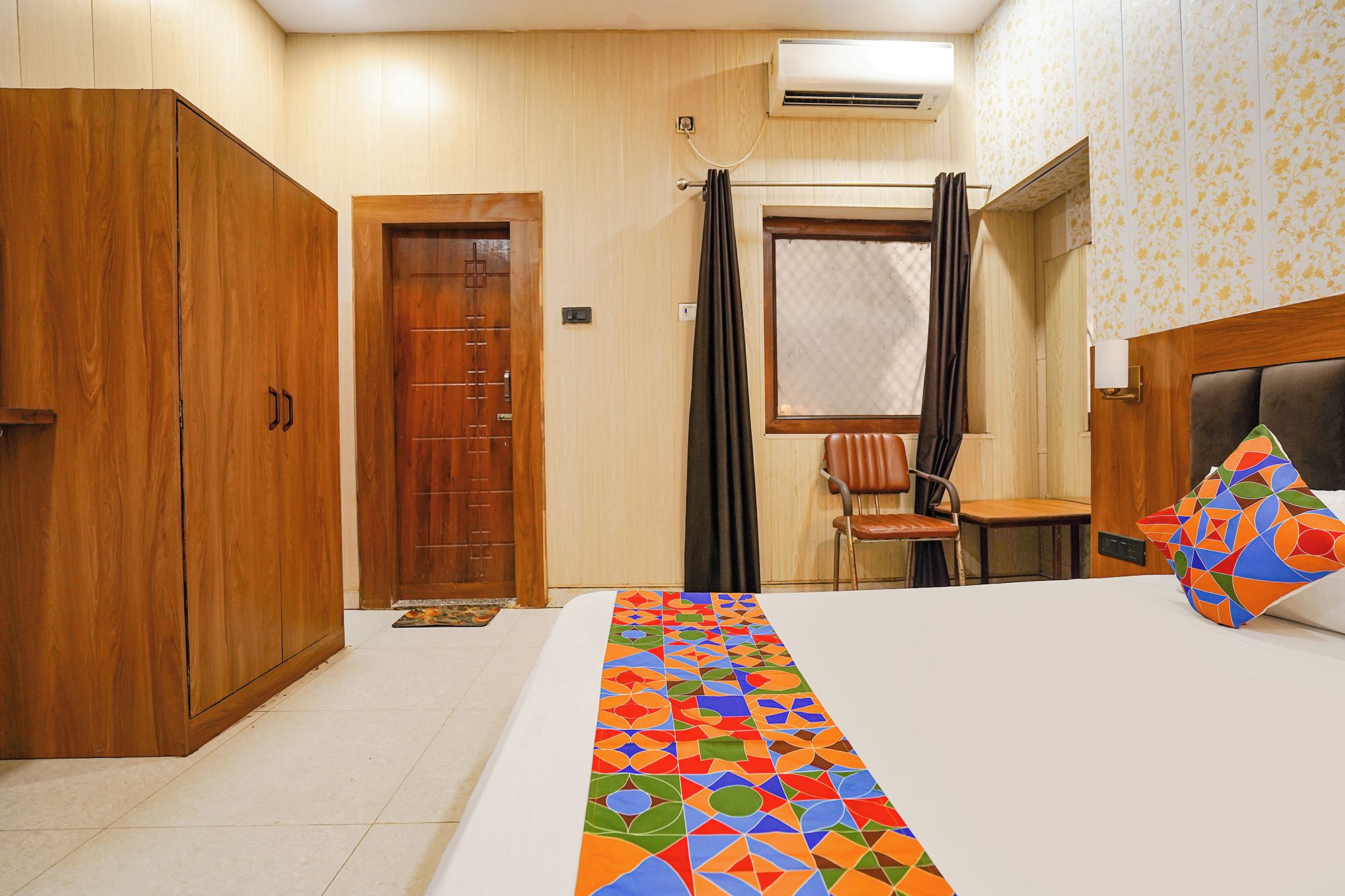 Een hotelkamer met een bed, een houten garderobe, een raam met gordijnen en een wandairconditioner.