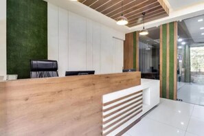 A reception desk with a wooden finish and a white counter. There are two black chairs and a green wall in the background.