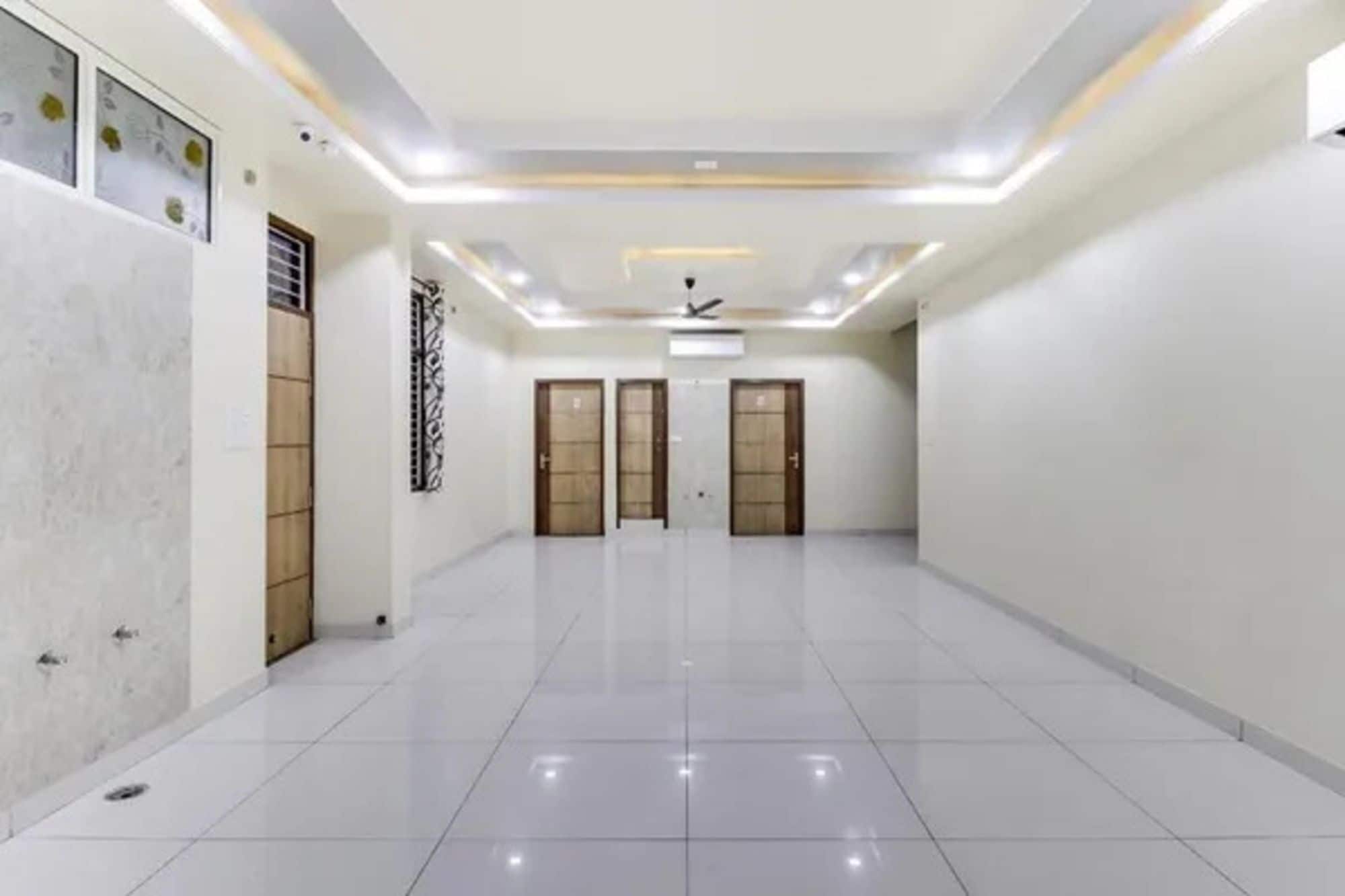 A spacious, well-lit hallway with a tiled floor, three wooden doors, and a ceiling fan.