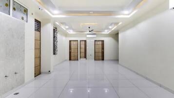 A spacious, well-lit hallway with a tiled floor, three wooden doors, and a ceiling fan.