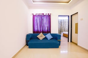 Una habitación con un sofá azul, una cortina estampada y una cama con edredón estampado.