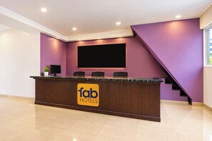 Una recepción con un cartel que dice 'fab hotels', un televisor de pantalla plana montado en la pared y una escalera que conduce a un nivel superior.