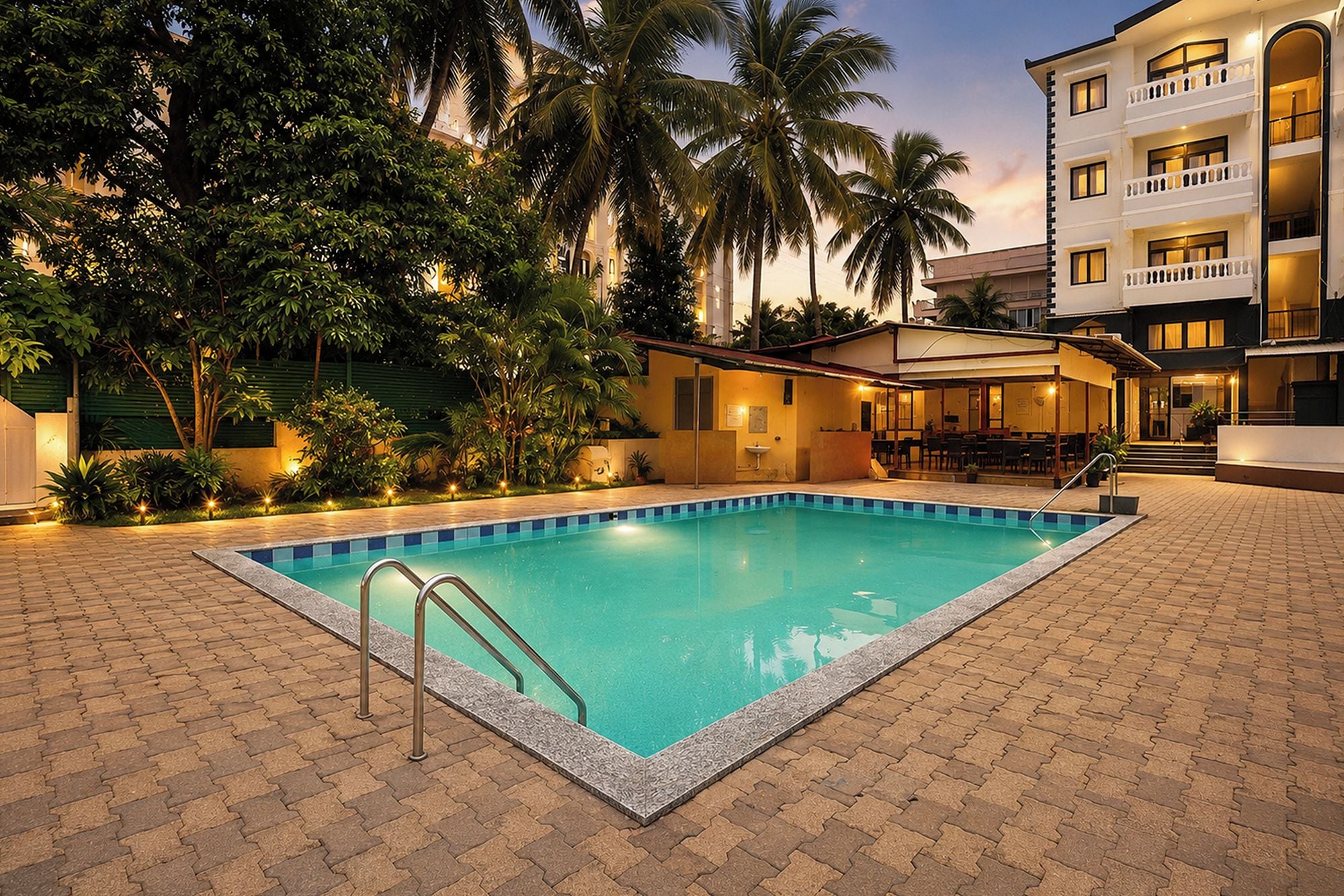 Una piscina con bordeado de baldosas, rodeada de palmeras y un edificio con varios pisos y balcones.