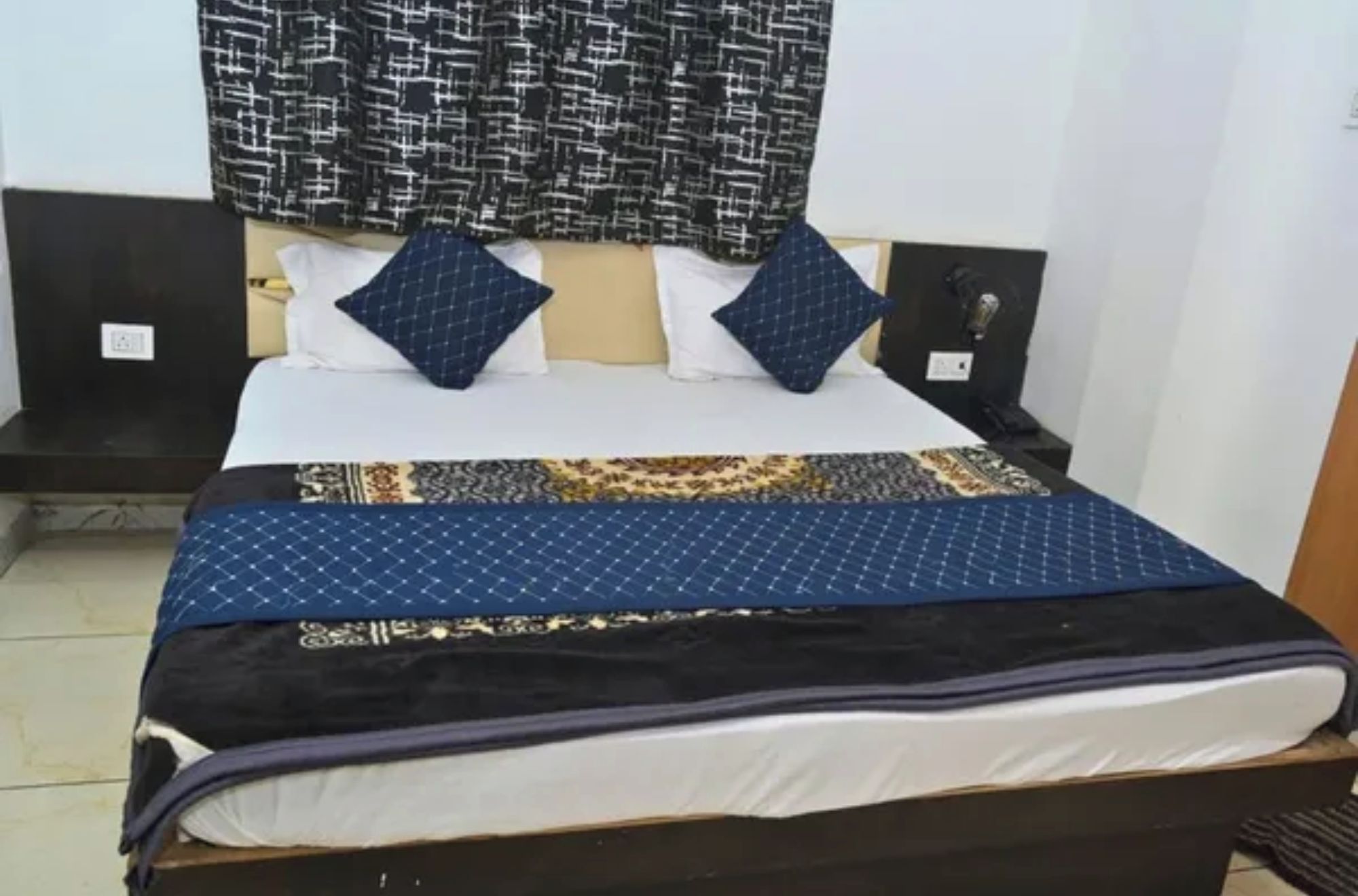 Una cama con una colcha estampada, dos almohadas y un cabecero con una cortina estampada arriba.