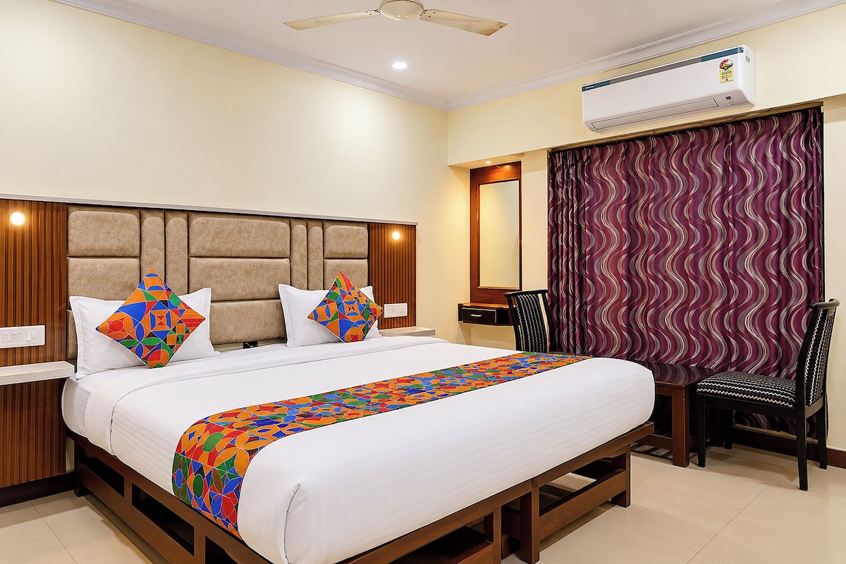 Habitación de hotel con cama, escritorio, silla, unidad de aire acondicionado y ventana con cortinas.