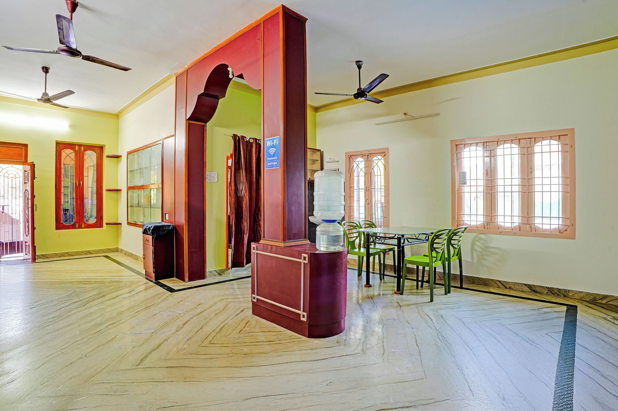 A hotel room with a large mirror, a water dispenser, a table with chairs, and ceiling fans.