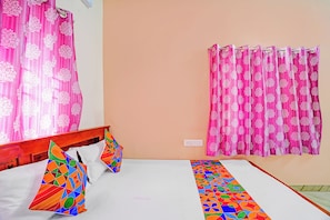A room with a bed, pillows, a window with curtains, and a wall socket.