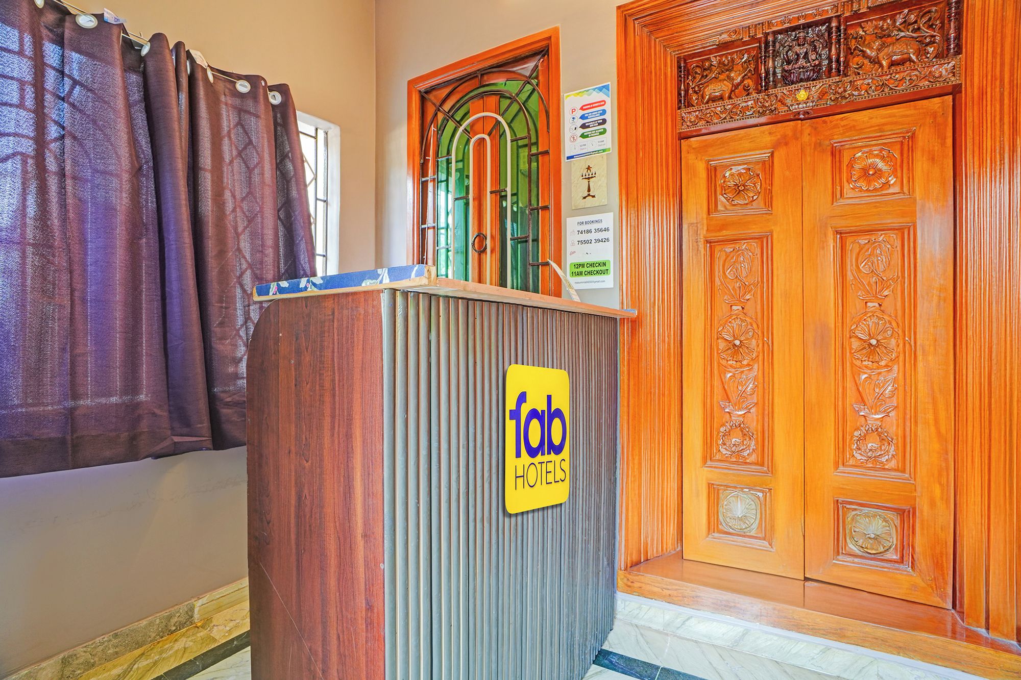 Recepção de hotel com balcão de madeira, um letreiro para 'Tab Hotels' e uma porta de madeira com entalhes elaborados.