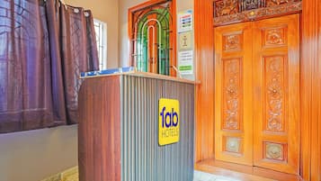 Recepção de hotel com balcão de madeira, um letreiro para 'Tab Hotels' e uma porta de madeira com entalhes elaborados.