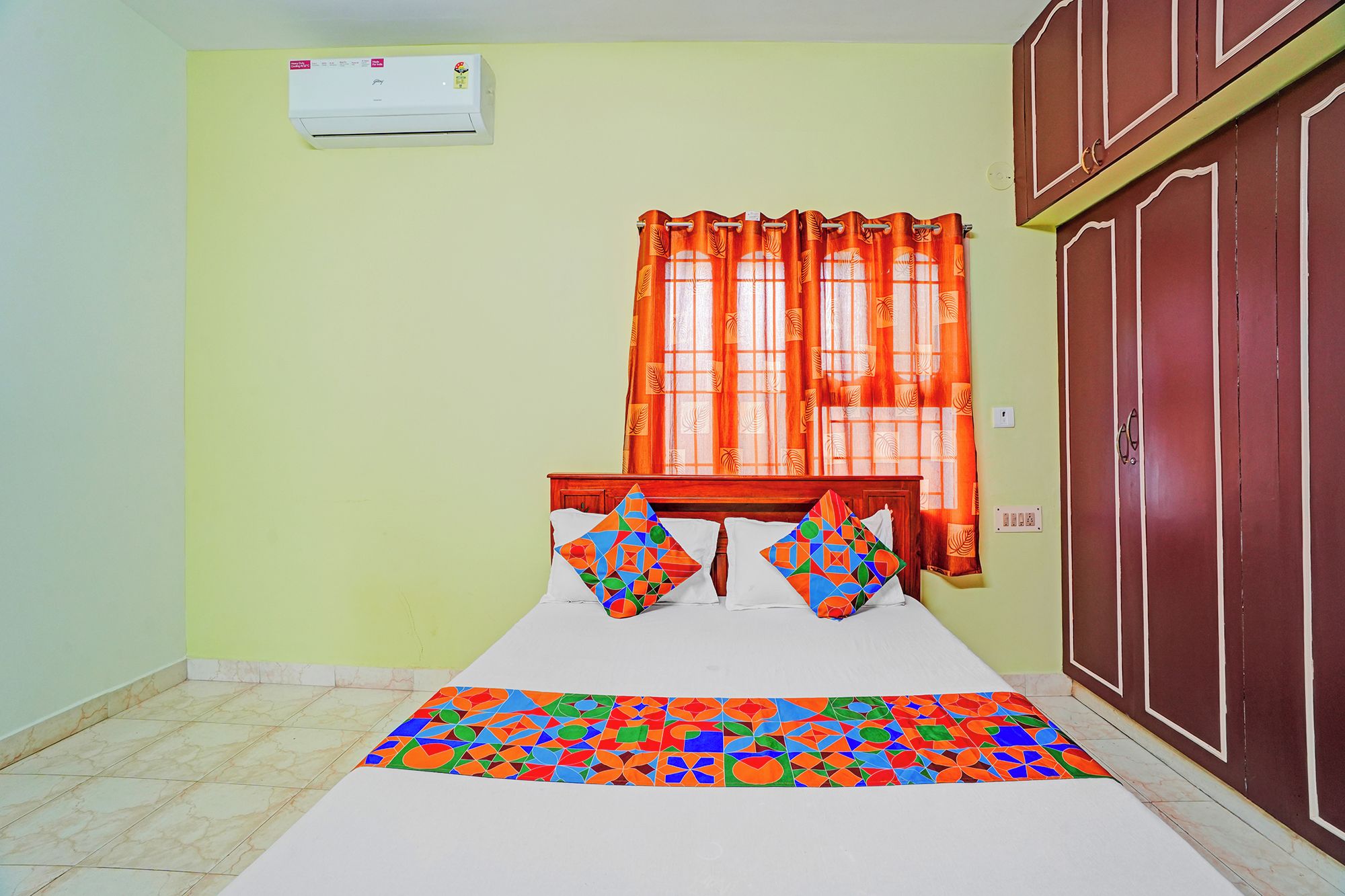 A room with a bed, a window with orange curtains, a wardrobe, and a tiled floor.