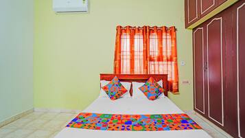 A room with a bed, a window with orange curtains, a wardrobe, and a tiled floor.