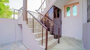 Escadaria com grades e corrimão de metal, que leva a uma porta com janela.