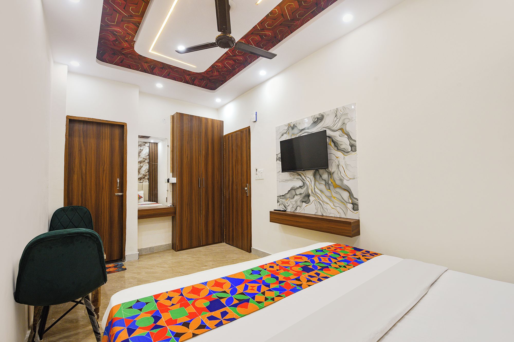 A bedroom with a bed, a desk, a chair, a wardrobe, a television, and a ceiling fan.