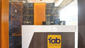 A hotel reception desk with a check-in/out sign, a digital screen, and a wooden panel wall.