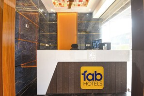 A hotel reception desk with a check-in/out sign, a digital screen, and a wooden panel wall. - FabHotel Metro Star (New Delhi)
