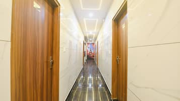 Corredor de hotel com portas de madeira, paredes de mármore e chão espelhado.