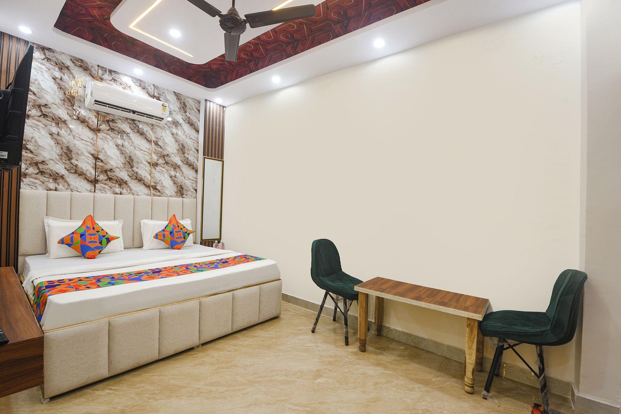 Un dormitorio con una cama, dos sillas, una mesita y aire acondicionado, además de un ventilador de techo.