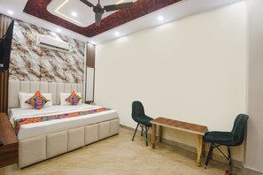 A bedroom with a bed, two chairs, a small table, an air conditioning unit, and a ceiling fan.