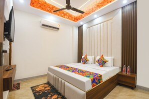 A modern bedroom with a bed, a ceiling fan, an air conditioning unit, and a wooden nightstand with bottles. - FabHotel Metro Star (New Delhi)