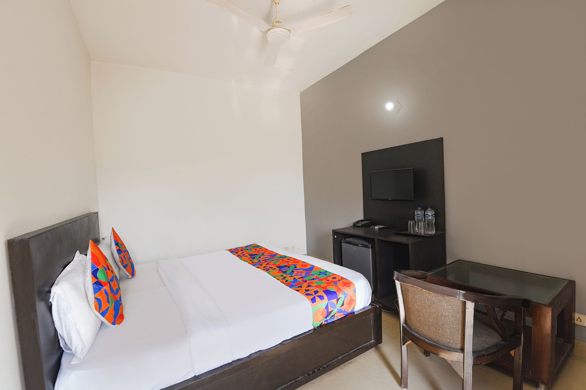 A hotel room with a bed, a desk, a chair, a television, and a refrigerator.