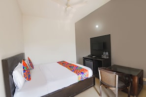 A hotel room with a bed, a desk, a chair, a television, and a refrigerator.