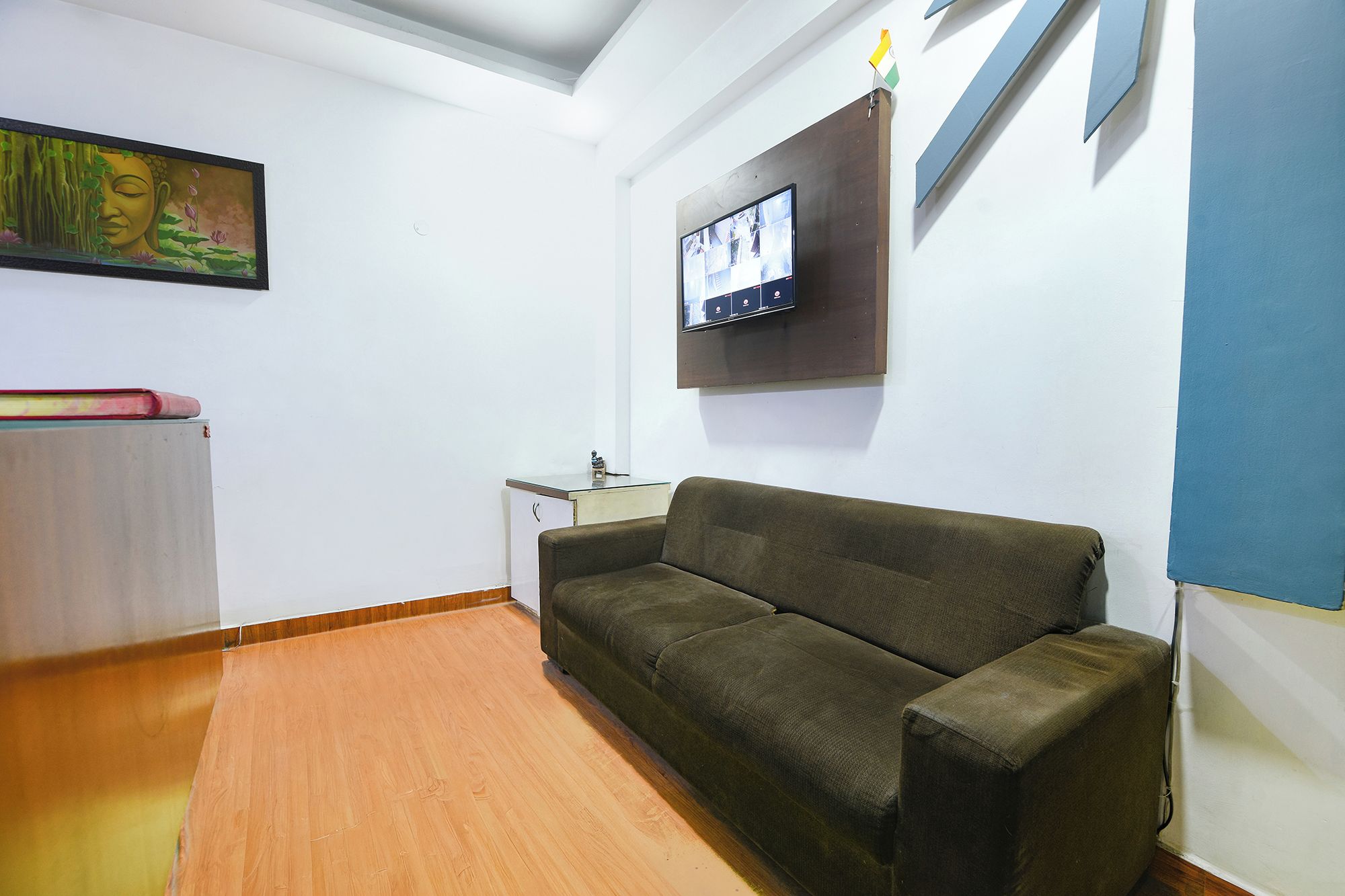 A room with a sofa, a television mounted on the wall, a painting, and a small table.