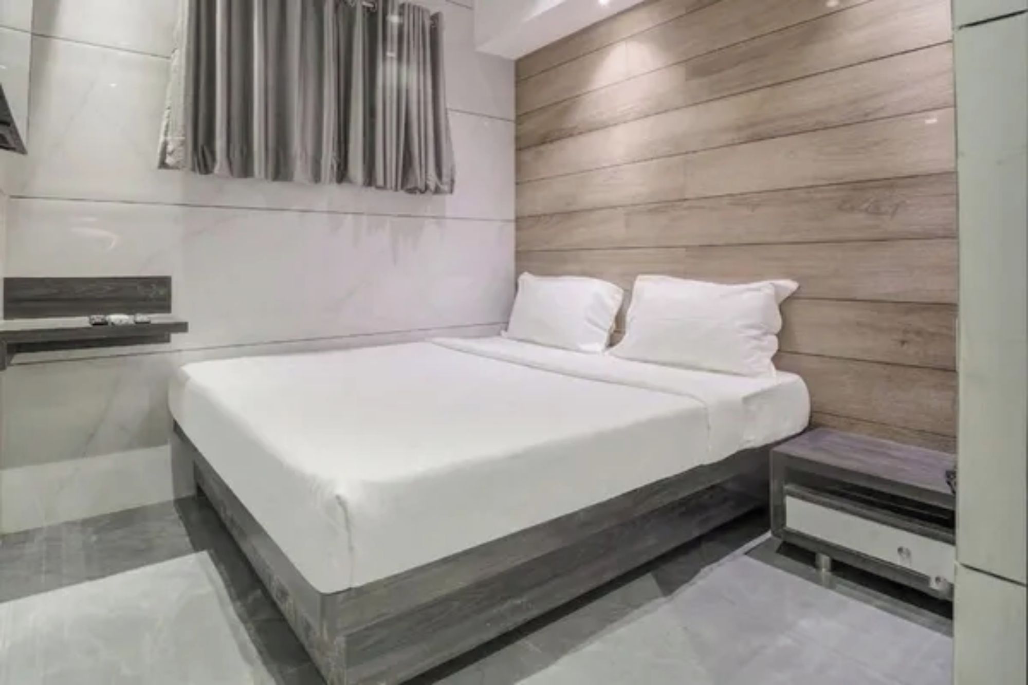 A modern bedroom with a wooden headboard, a large bed with white bedding, a bedside table, and a built-in bench.