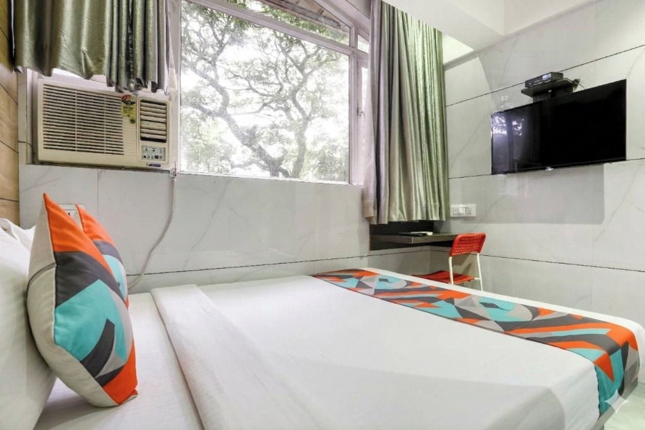 A hotel room with a bed, a desk, a TV, and a window with curtains.