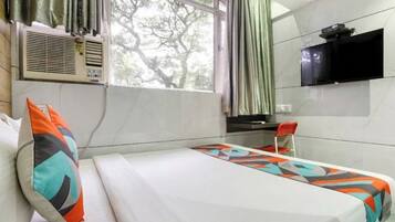 A hotel room with a bed, a desk, a TV, and a window with curtains.