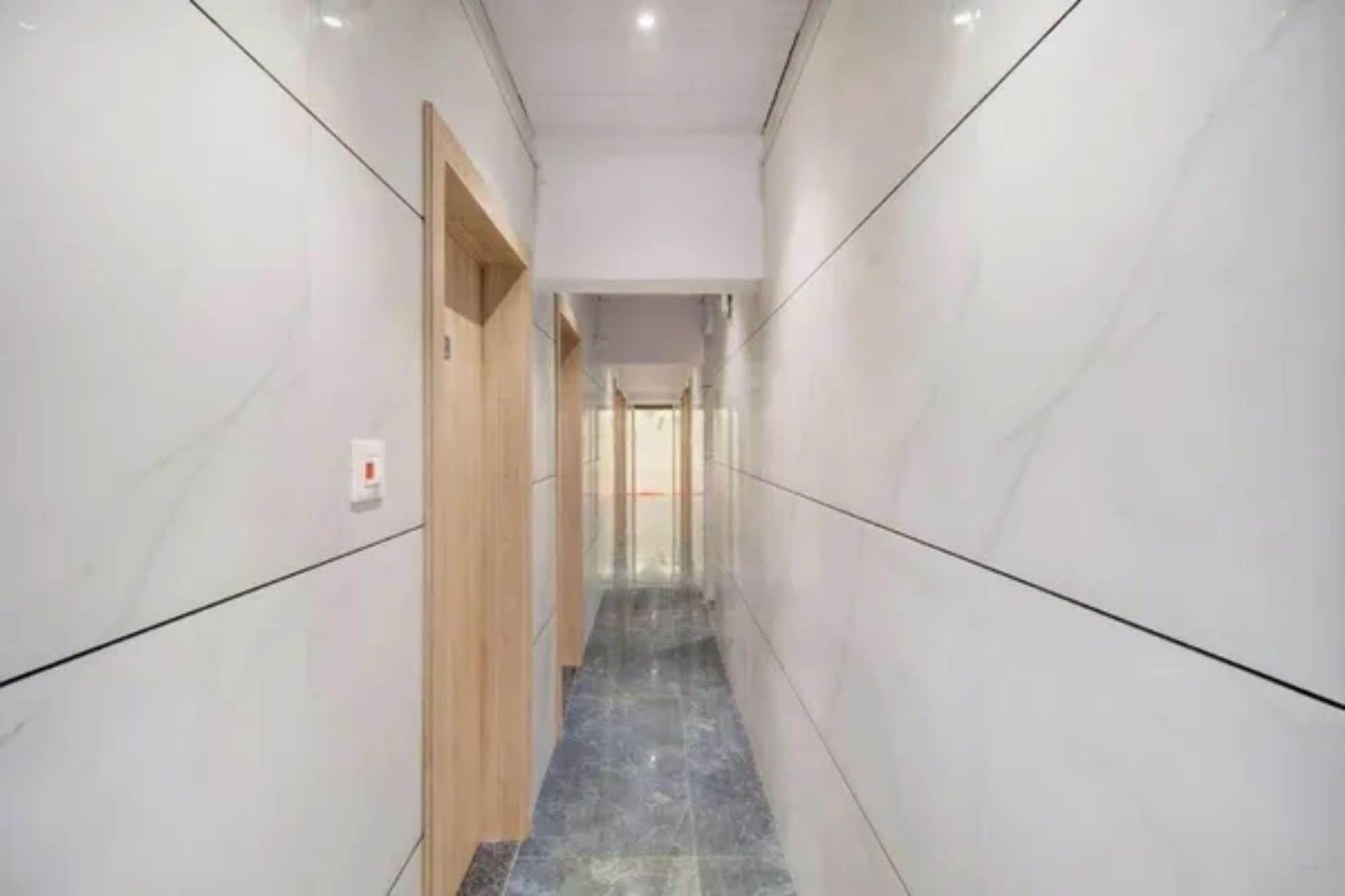 A corridor with white walls and a marble floor, leading to a door at the end.