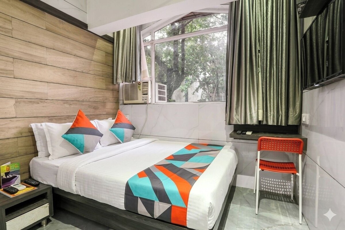 A hotel room with a bed, a nightstand, a chair, and a window with curtains.