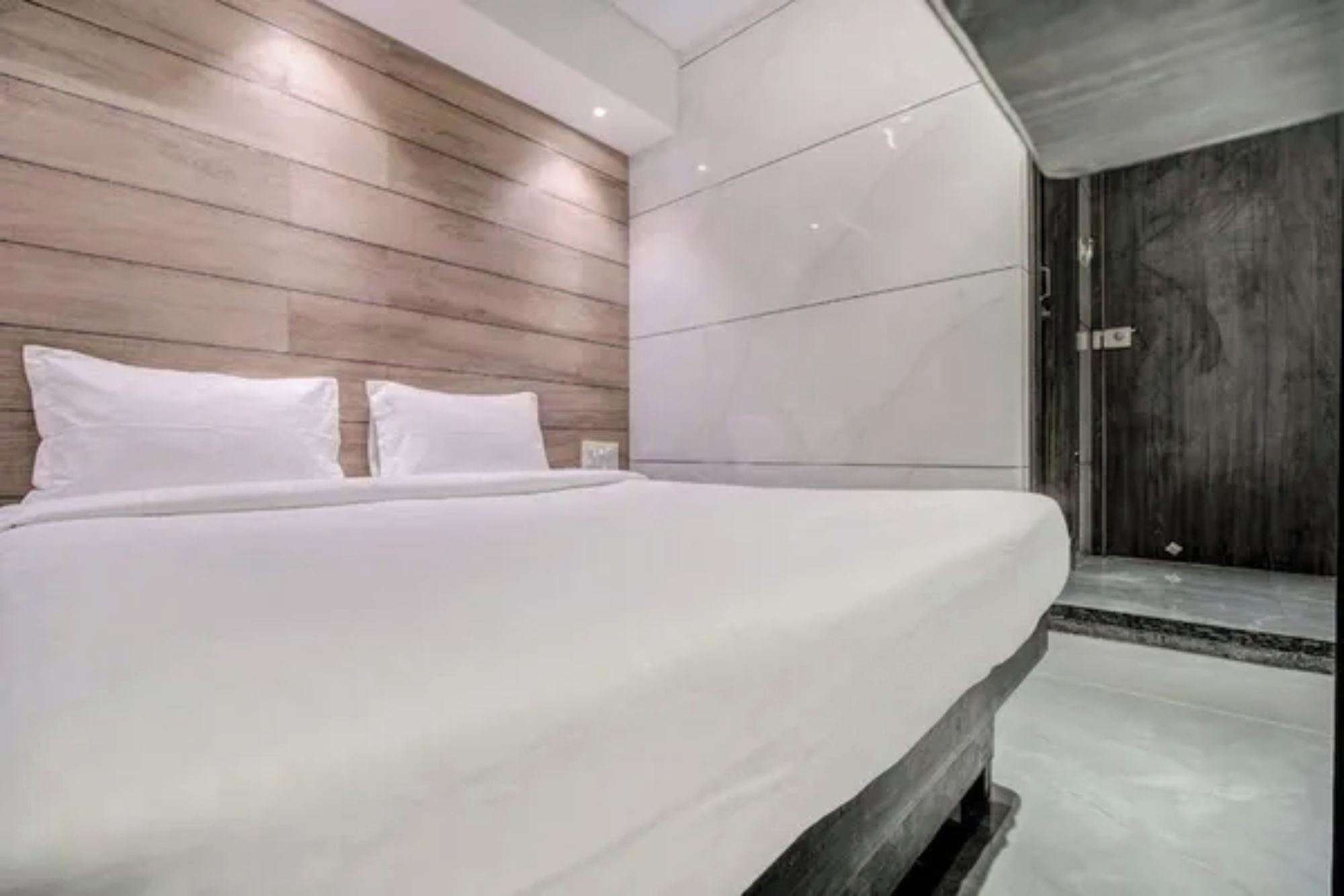 Une chambre moderne avec un grand lit, une tête de lit en bois et une porte sombre.