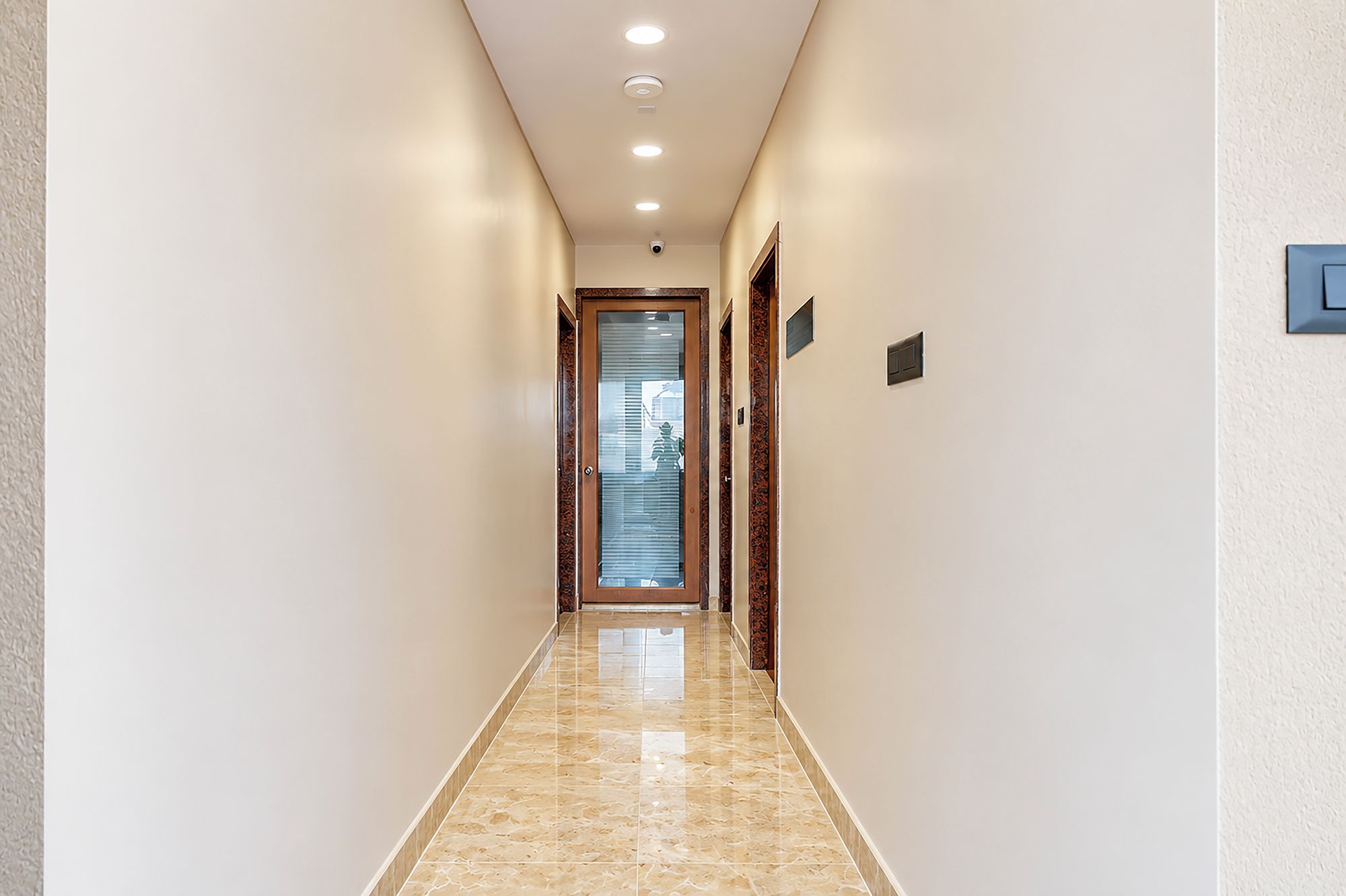 A hallway with a marble floor, recessed ceiling lights, and a door at the end.
