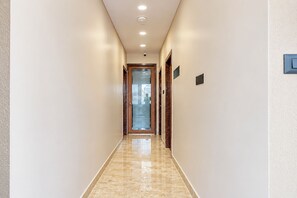 Un pasillo con piso de mármol, luces empotradas en el techo y una puerta al final.
