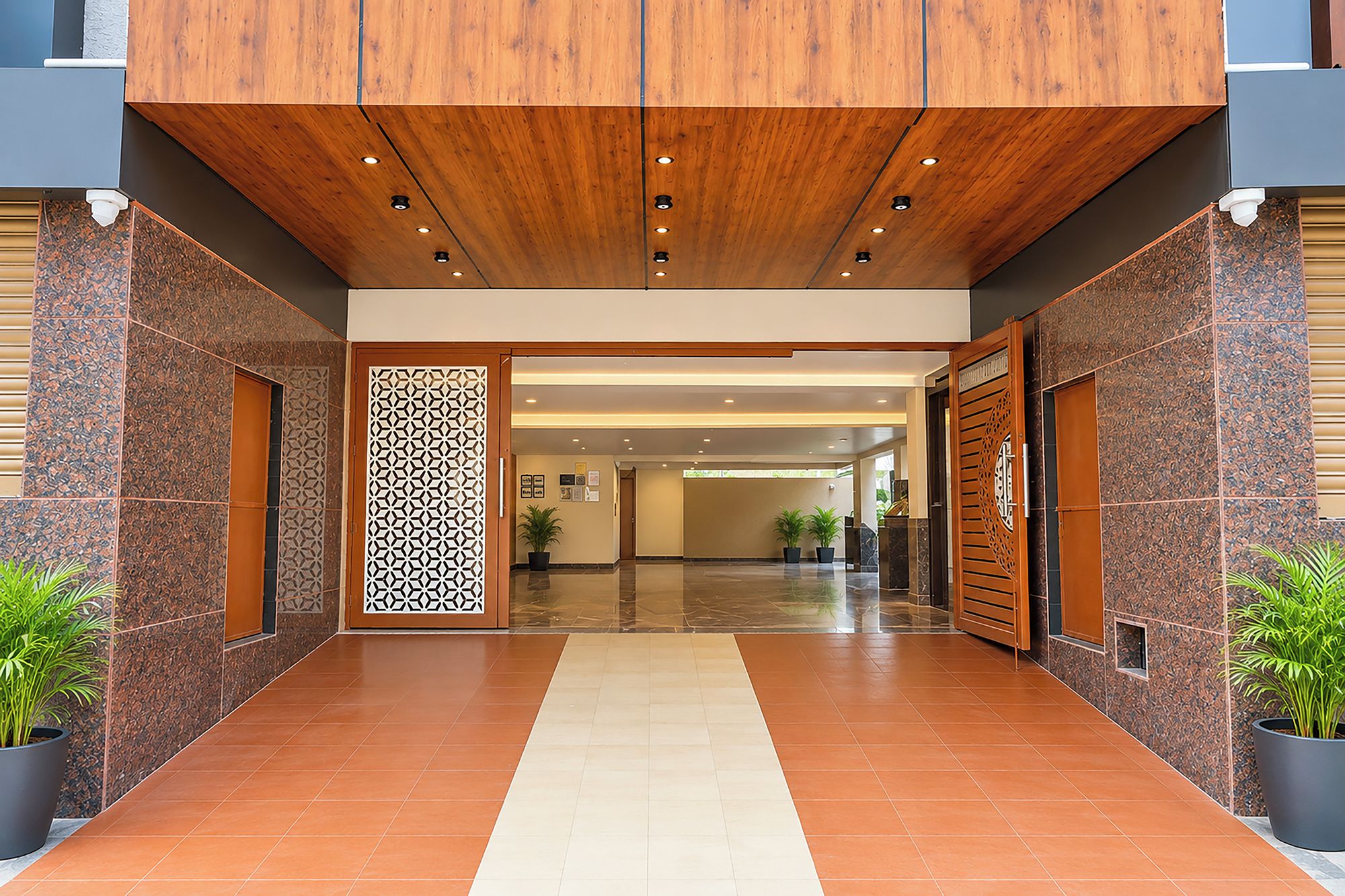 A hotel entrance with a wooden ceiling, a decorative wall panel, and potted plants.