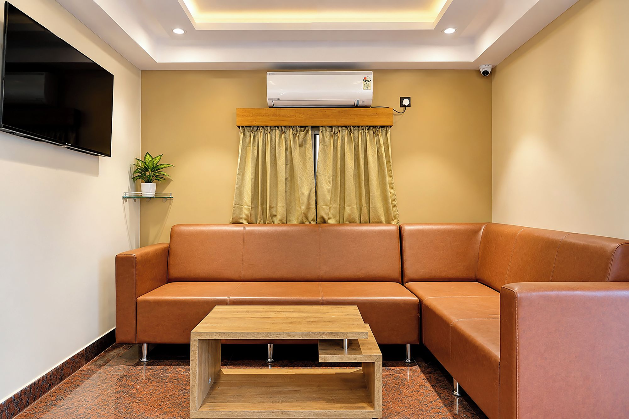 Una sala moderna con un sofá de cuero, una mesa de centro de madera, un aire acondicionado, un televisor y una planta en maceta.