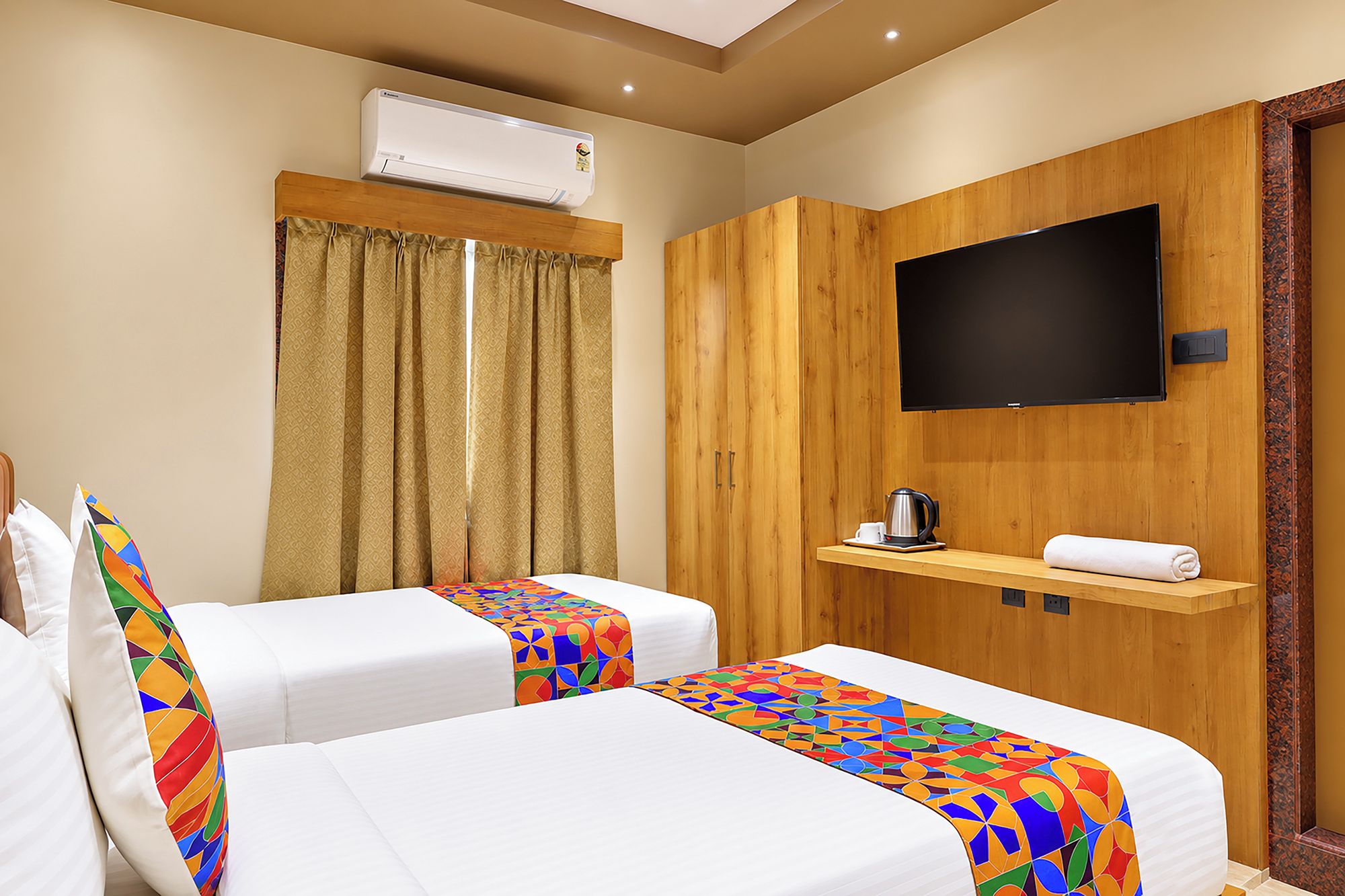 A hotel room with two beds, a television, a coffee maker, and an air conditioning unit.