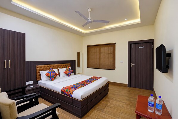 A hotel room with a bed, bedside table, chair, TV, and a ceiling fan.